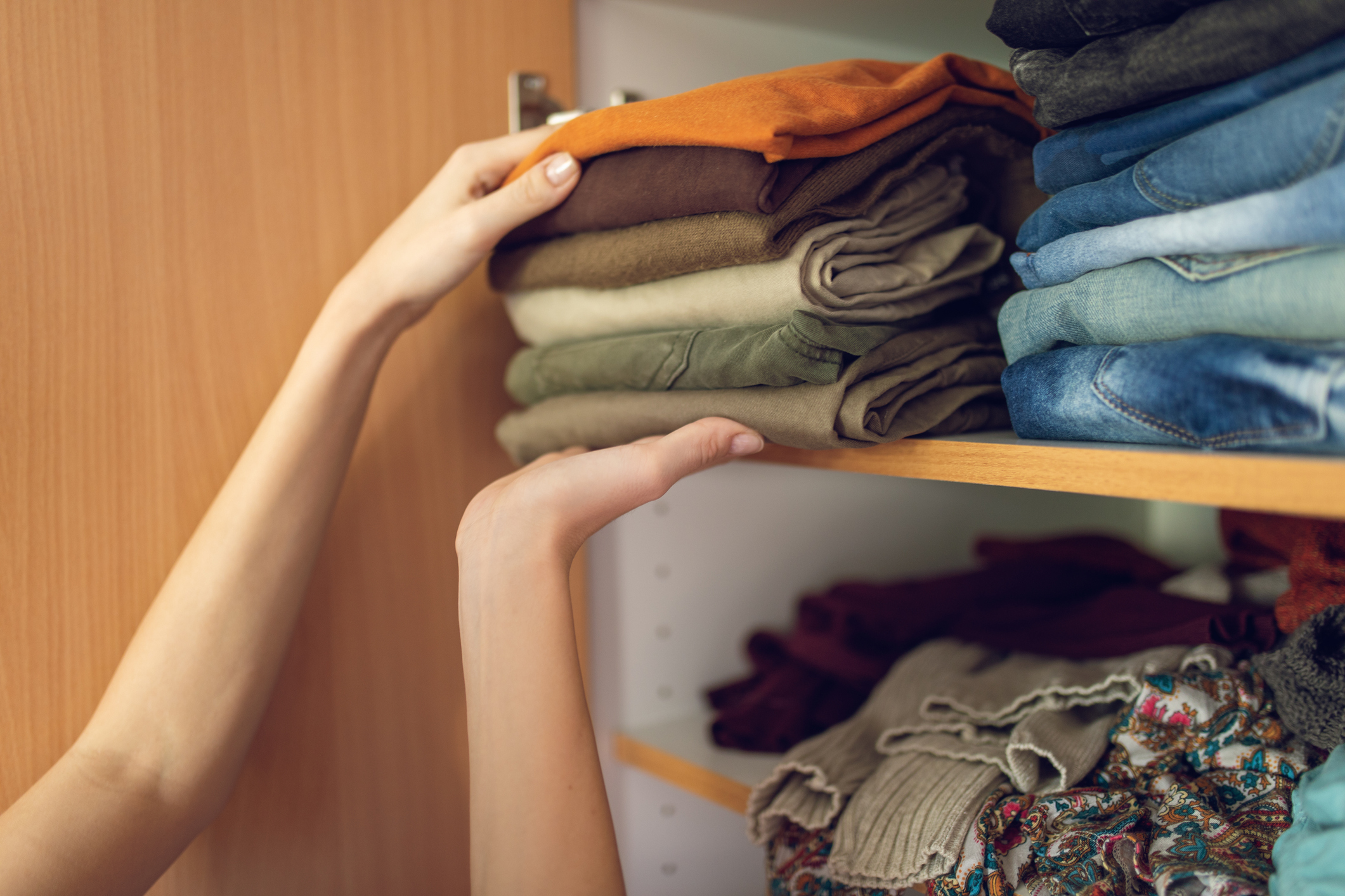 Hands putting a pile of folded t-shirts into a wardrobe