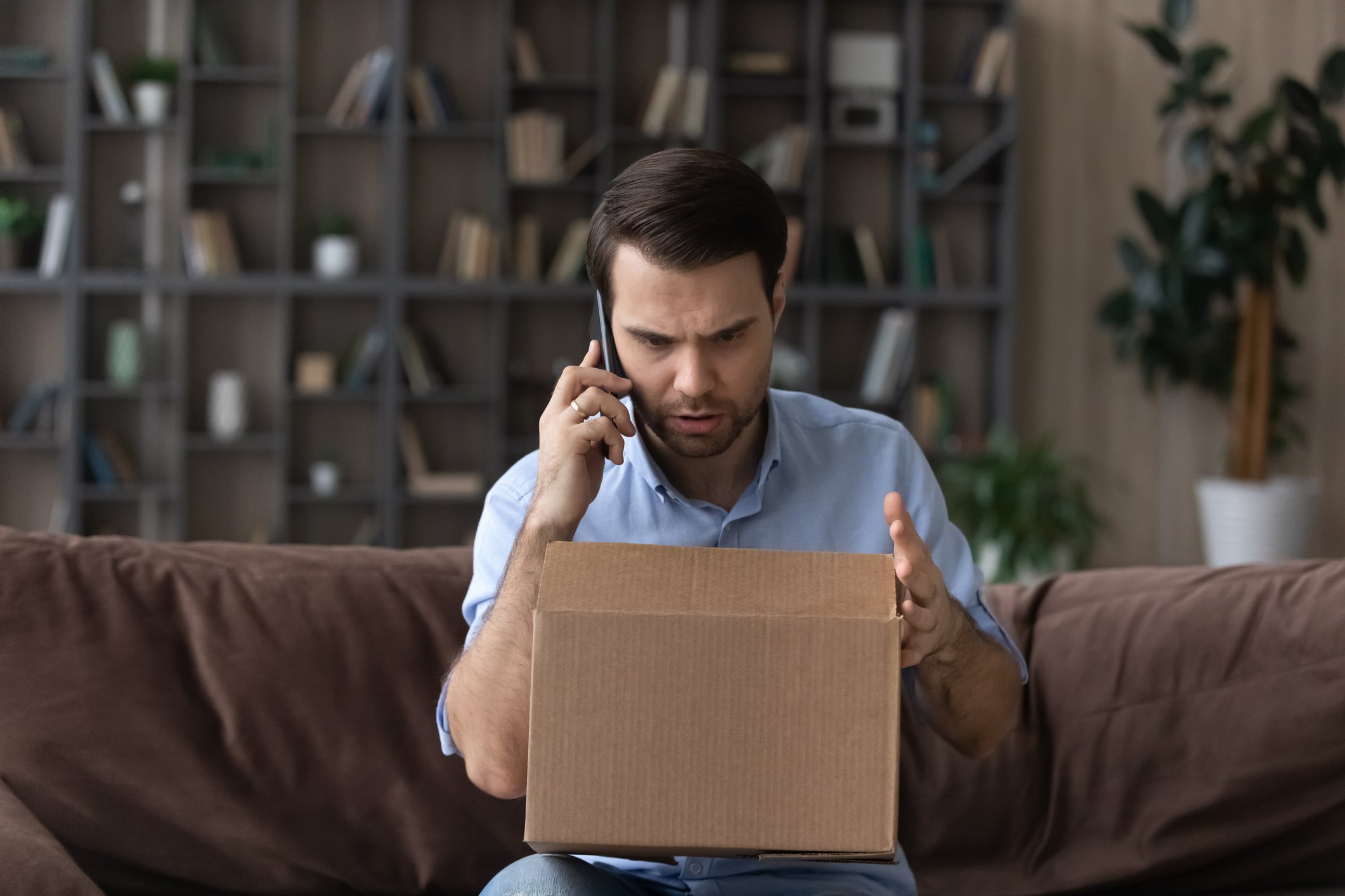 man stressed while on phone and holding parcel
