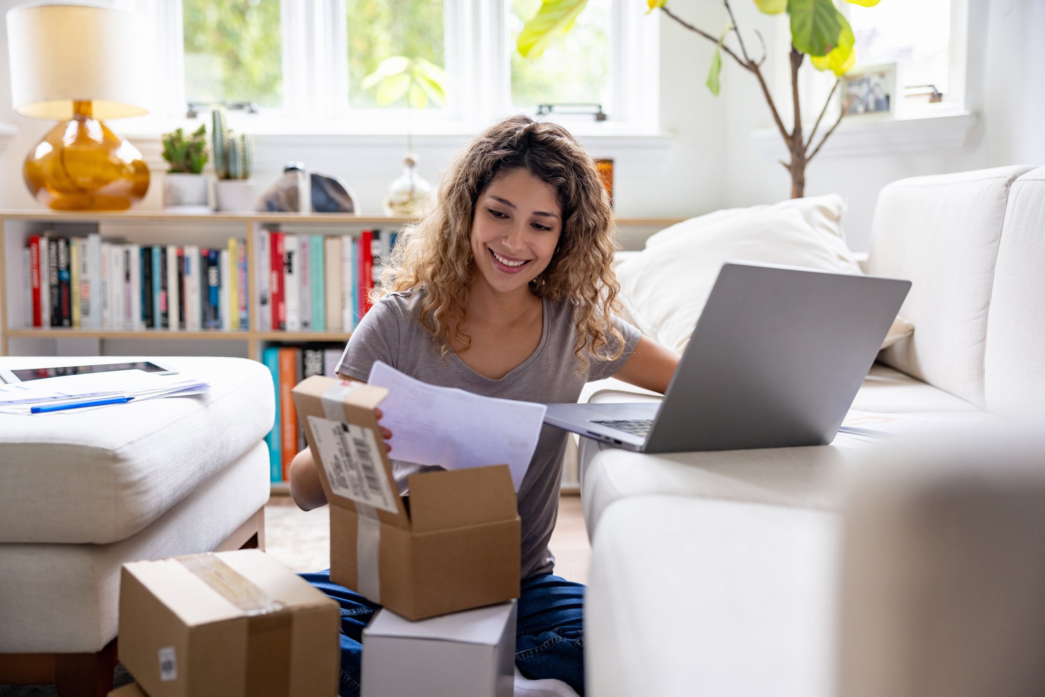 woman opening parcel at home while using laptop