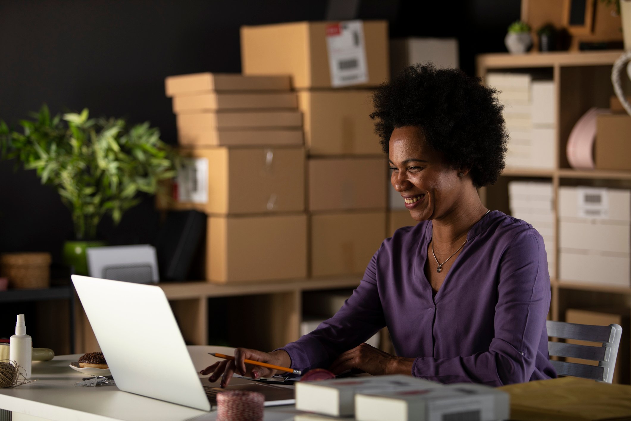 Woman smiling at laptop with boxes in background