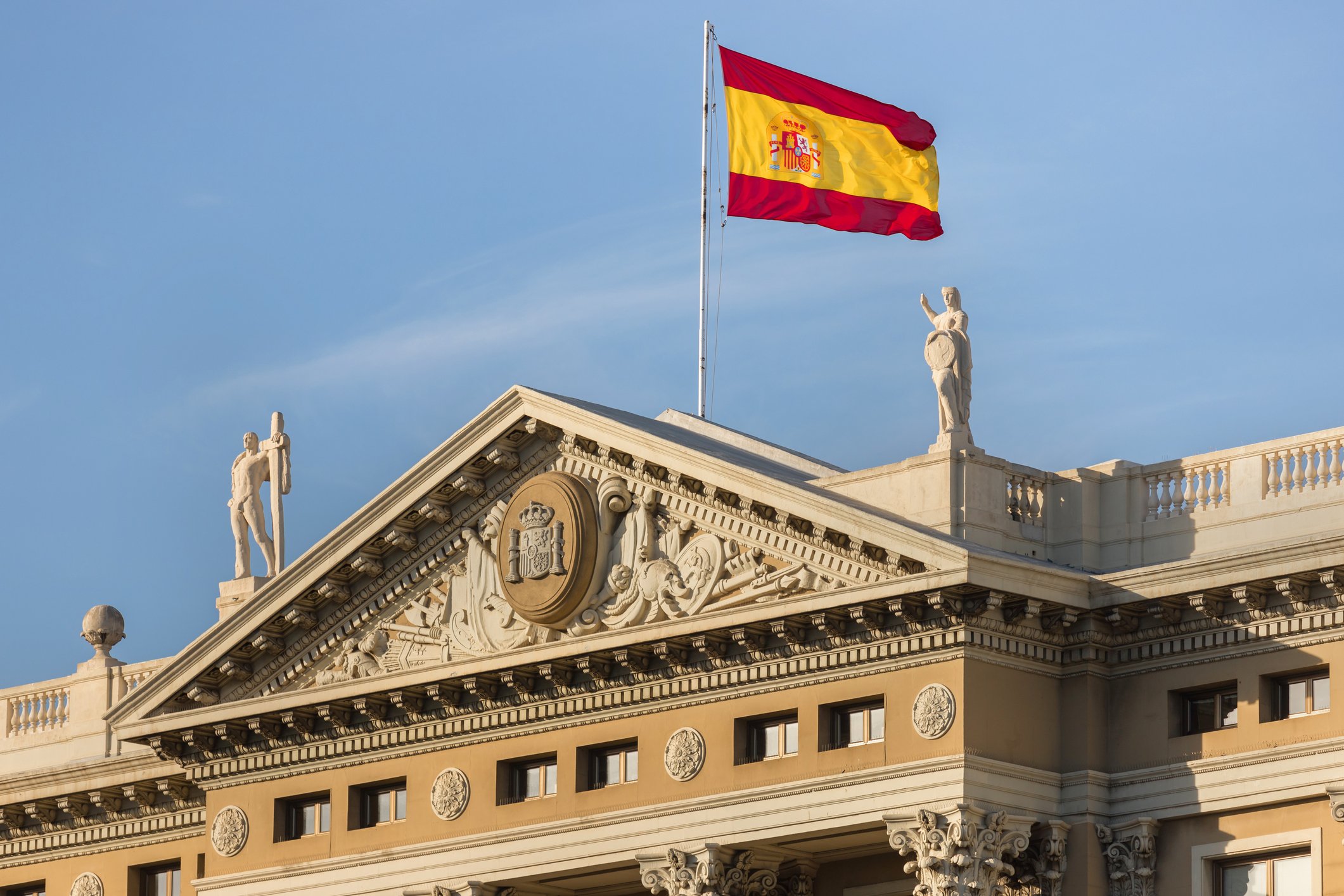 DSpanish flag waving against a blue sky over a government building