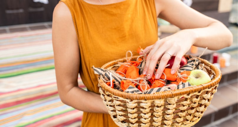 Woman holding a wicker basket containing wrapped items and apples