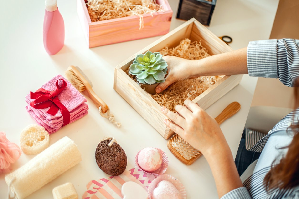 Woman packaging a wooden box with gifts such as a plant and soaps