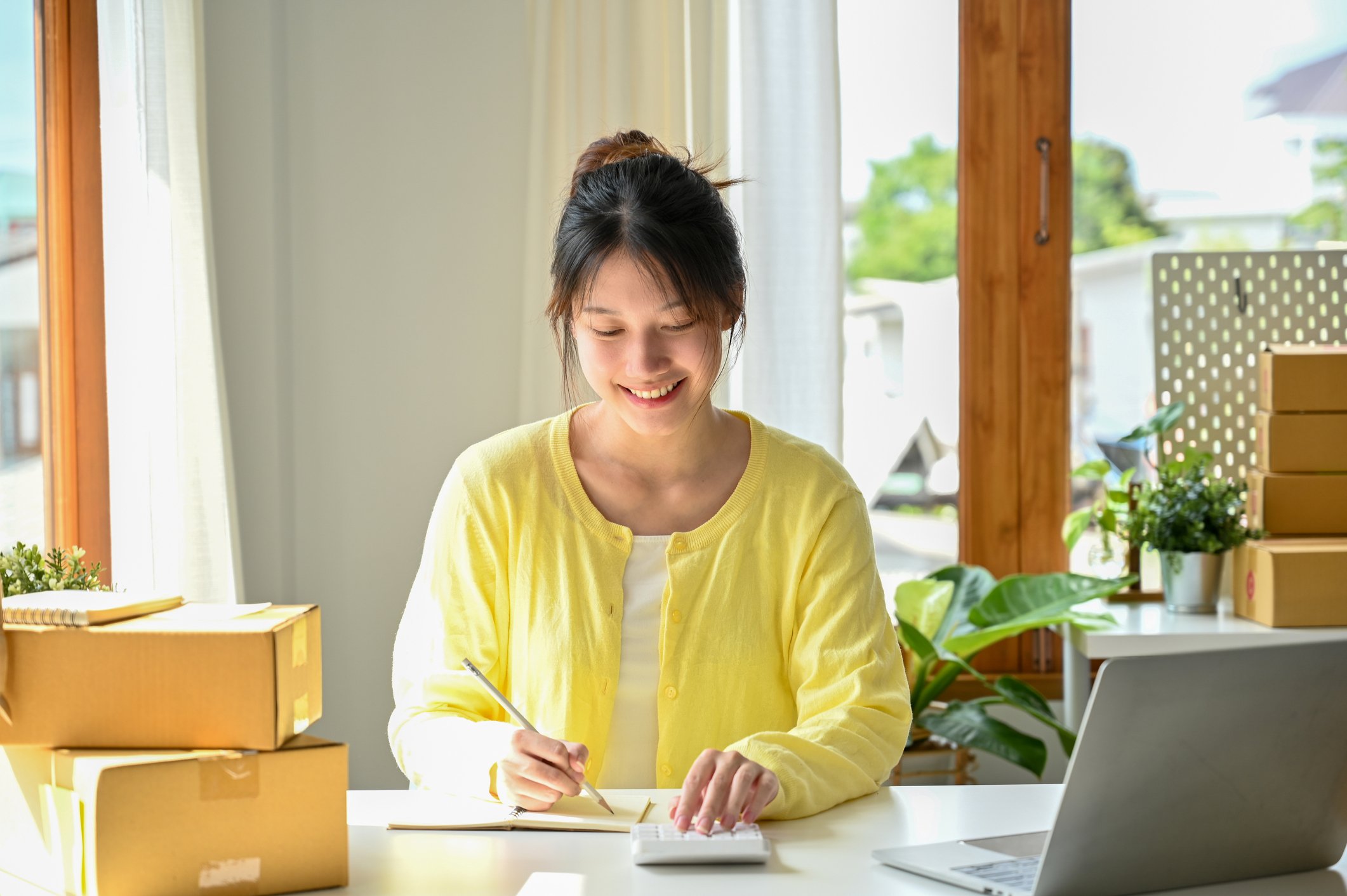 woman writing on paper with parcels on table