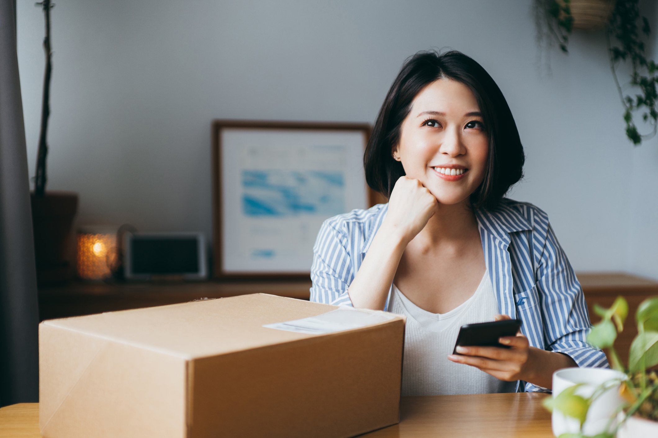 woman thinking while holding phone and parcel on table