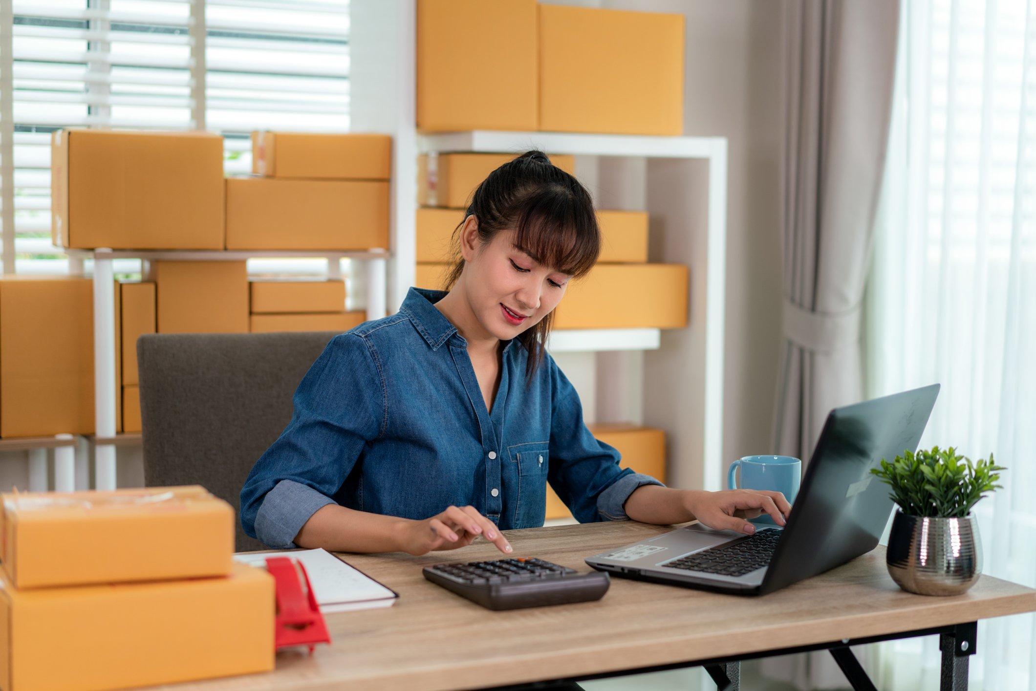 woman using calculator while on laptop with parcels in background